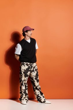 Yakışıklı genç bir adam kendine güvenerek duruyor, kalın turuncu bir duvara karşı moda anlayışını sergiliyor..
