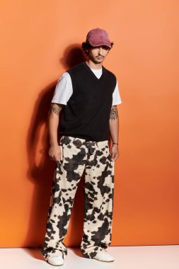 Yakışıklı genç adam turuncu bir arka plana karşı duruyor, modern tarzı sergiliyor..