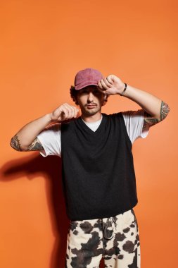 Yakışıklı genç bir adam eşsiz moda anlayışını koyu turuncu bir ortamda sergiliyor..