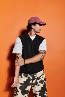Modaya uygun genç bir adam kendine güvenen bir duruş sergiliyor, moda kıyafetlerini ve sanatsal dövmelerini sergiliyor..
