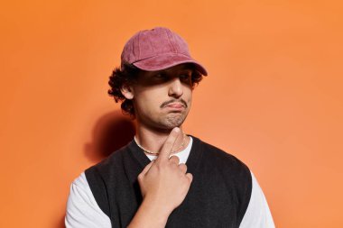 Moda şapkalı şık bir genç adam parlak turuncu bir duvarın önünde düşüncelerini tartıyor..