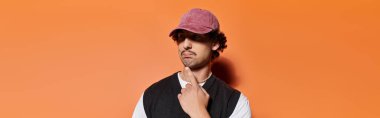 Şık şapkalı yakışıklı genç adam modern modayı gösterirken düşünceli bir şekilde poz veriyor..