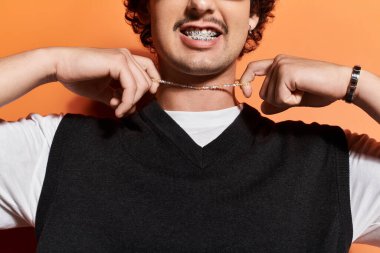 Kendine güveni tam bir genç adam takılarını, çarpıcı bir arka plana karşı neşeli bir gülümsemeyle sergiliyor..