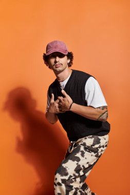 Yakışıklı bir genç, turuncu bir duvarın önünde neşeli bir poz verirken cazibesini sergiliyor..