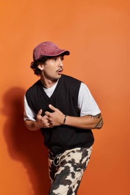 Moda kıyafetleri içinde şık bir genç adam canlı turuncu bir arka plana karşı güvenle duruyor..