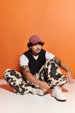 Yakışıklı genç bir adam yerde otururken moda anlayışını sergiliyor ve kendine güvenini gösteriyor..