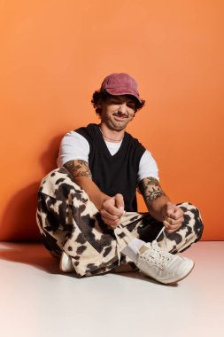 Yakışıklı genç adam yerde dinleniyor, modaya uygun bir kıyafet giyiyor ve gülümsüyor..
