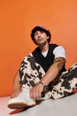 Yakışıklı genç adam rastgele poz veriyor, koyu turuncu arka plana karşı eşsiz moda seçimini vurguluyor.