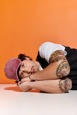 Yakışıklı genç bir adam moda anlayışını ve çarpıcı dövmelerini sergileyerek bir yüzeyde rahatlar..