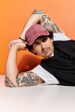 Moda kıyafetli yakışıklı genç adam dikkat çekici bir turuncu arka planla tesadüfen dinleniyor..