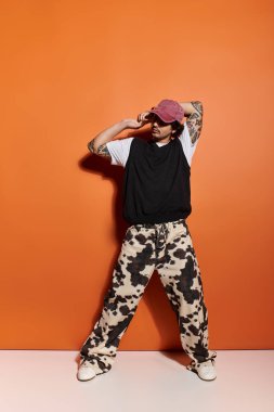 Tarz sahibi genç bir adam sanatsal bir arkaplan karşısında günlük moda sokak kıyafetlerinde poz veriyor..