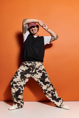 Kendine güvenen genç adam dinamik bir duruşta cesur turuncu arkaplanlı şık kıyafetler sergiliyor..