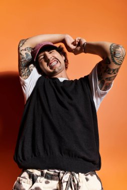 Yakışıklı genç bir adam neşe içinde, şık kıyafetlerini ve canlı dövmelerini sergiliyor..
