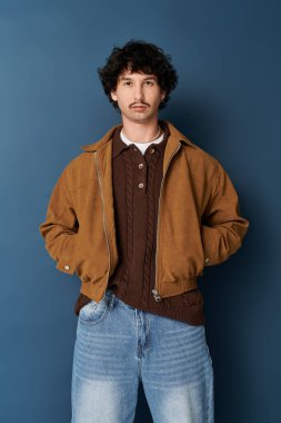 Yakışıklı genç adam, kendine güveni tam bir mavi zemin üzerinde, modern moda titreşimleri yayıyor.