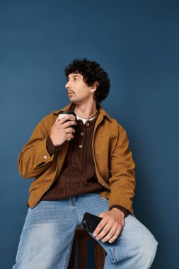Şık bir genç adam, hayat dolu mavi bir fonda otururken rahatlar ve kahvesinin tadını çıkarır..