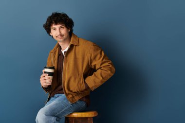 Kıvırcık saçlı yakışıklı genç bir adam kahve fincanı tutuyor ve modern bir ortama güveniyor..