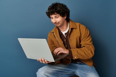 Dizüstü bilgisayar kullanarak, odak ve coşku gösteren, modaya uygun giyinmiş yakışıklı bir genç..