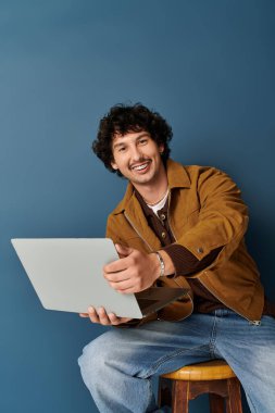 Yakışıklı genç adam dizüstü bilgisayarı üzerinde çalışırken gülümsüyor, modern moda sergiliyor..