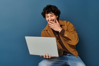 Yakışıklı genç adam gündelik oturuyor, gülümsüyor ve son moda bir ortamda dizüstü bilgisayarıyla meşgul oluyor..