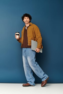 Kahve fincanı ve dizüstü bilgisayarı olan şık bir genç adam yaratıcı bir güven yayar..