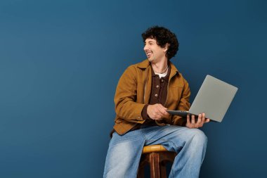 Yakışıklı genç adam bir taburede oturmuş, dizüstü bilgisayarıyla meşgul oluyor ve anın tadını çıkarıyor..