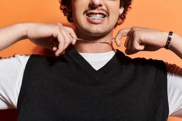 Kendine güveni tam bir genç adam takılarını, çarpıcı bir arka plana karşı neşeli bir gülümsemeyle sergiliyor..