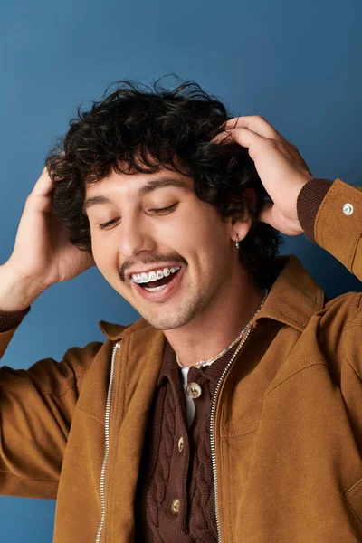 Yakışıklı genç bir adam saçını düzeltirken gülümsüyor, şık kıyafetini gösteriyor..