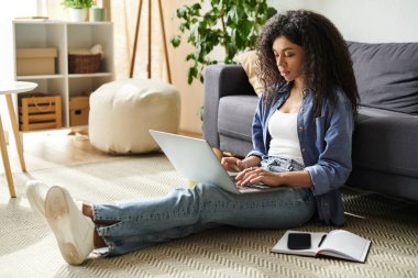 Genç bir Afrikalı Amerikalı kadın evdeki şık oturma odasından verimli bir şekilde çalışıyor..