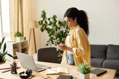 Genç bir Afrikalı Amerikalı kadın telefonunu kontrol ederken şık evinde çalışıyor..