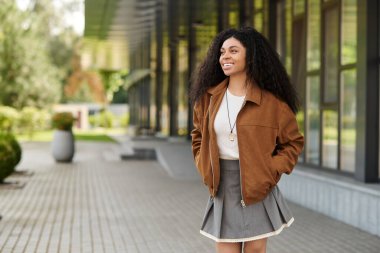Kendine güvenen genç bir kadın, süet ceket ve etekle şık bir sonbahar elbisesi içinde gülümsüyor..
