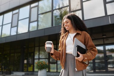 Kıvırcık saçlı güzel bir kadın kahveyle gülümserken sonbahar kıyafeti giyer..