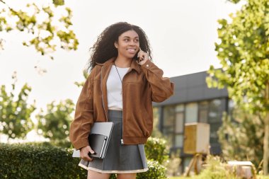 Süet ceketli ve etekli neşeli genç bir kadın açık havada sonbahar gününün tadını çıkarıyor..