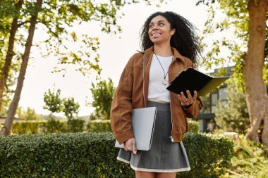 Süet ceketli ve etekli genç bir kadın, sonbaharın tadını çıkarıyor. Kitaplar ve dizüstü bilgisayarla..