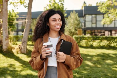 Kıvırcık saçlı genç bir kadın, güzel bir sonbahar ortamında gülümserken kahve fincanı tutuyor..