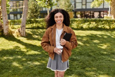 Genç siyah bir kadın dışarıda güneşli bir günün tadını çıkarırken şık bir sonbahar kıyafetiyle neşe saçıyor..