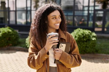 Güzel genç bir kadın elinde kahve tutarken ve şık bir sonbahar kıyafeti giyerken gülümsüyor..