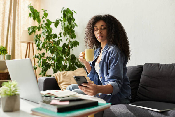 Молодая афроамериканка наслаждается утренним кофе, работая удаленно в уютной квартире.