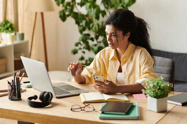 A focused young woman works from her modern apartment, balancing tasks on her laptop and phone.