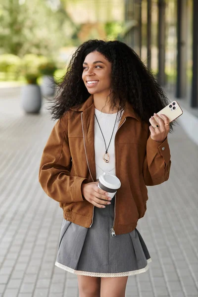 Kıvırcık saçlı genç bir kadın sonbahar kıyafetine güvenir ve gününün tadını çıkarır..