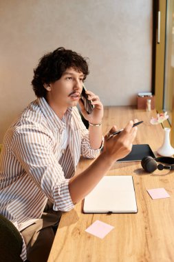 Yakışıklı genç adam, bir kafede notlar alırken telefonda konuşuyor..