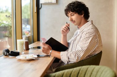 Yakışıklı genç bir adam büyüleyici bir kafede oturuyor ve yakınlarda bir içkiyle notlar alıyor..