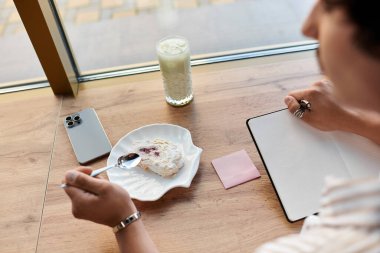 Yakışıklı genç adam sıcak bir kafe atmosferinde soğuk bir içecek yudumlarken tatlının tadını çıkarıyor..