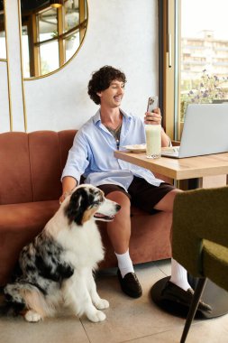 Yakışıklı genç bir adam kafeterya atmosferinin keyfini çıkarıyor, köpeğini okşarken dizüstü bilgisayarıyla çalışıyor..