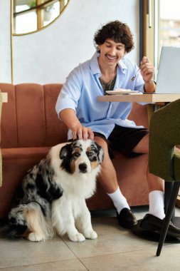 Genç adam bir kafede rahatlıyor, yanında sevimli bir köpekle mutlu bir şekilde bağ kuruyor..