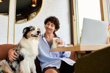 Yakışıklı genç adam rahat bir kafede rahatlar, köpeğiyle kaynaşırken bir yudum içer..