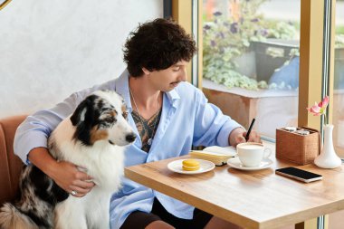 Sadık köpeği yanında otururken genç bir adam kafede vakit geçirmekten zevk alıyor..