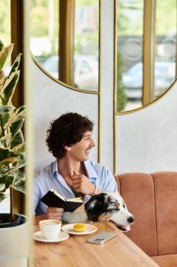 Genç bir adam, rahat bir kafede, yanında köpeğiyle yazarak keyifli bir anın tadını çıkarıyor..