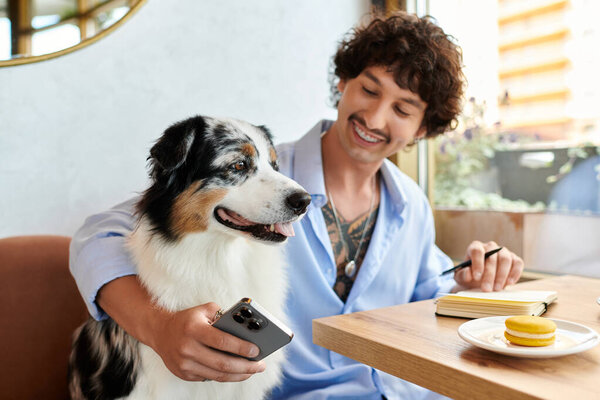 Молодой человек улыбается, сидя в уютном кафе, делясь мгновениями со своей собакой и записками.