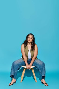 Kendine güvenen bir kadın, parlak mavi bir arka plana karşı sandalyede poz verir..
