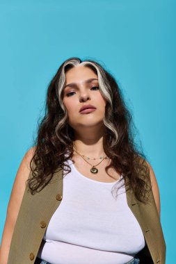 Zarif bir kadın eşsiz bir güzellik ve özgüven sergiliyor, cesur mavi bir arka planın önünde duruyor.